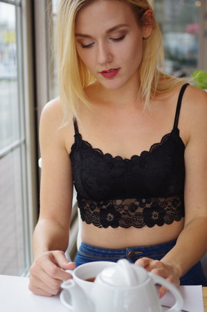 Portrait of a blond girl in a black lace crocheted top and jeans. Street Cafe. In the foreground is a white teapot and a cup of tea.の写真素材