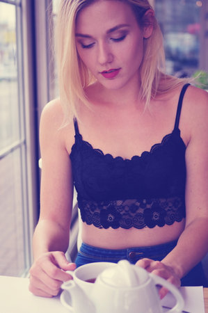 Portrait of a blond girl in a black lace crocheted top and jeans. Street Cafe. In the foreground is a white teapot and a cup of tea.の写真素材