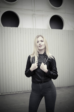 Playful mood of a beautiful young girl while walking around the city. Urban background. Black handbag on the shoulder. She is dressed in a black jacket and blue jeans.の写真素材
