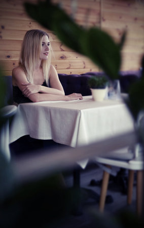 Beautiful blonde girl posing while sitting in a cozy cafe. She wears a black lace tops and blue jeans. on purple sofa, game peeping, the global march, active woman seriesの写真素材