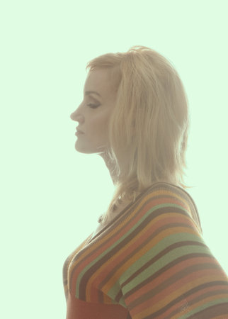 Blonde women in backlight,1960 - 1970 style, profile. She is dressed in a knitted blouse in a strip, on her neck she has a beautiful necklace. A clean white background. Isolated image. Side view.の写真素材