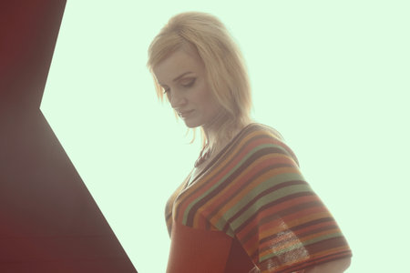 Blonde women in backlight,1960 - 1970 style She is dressed in a knitted blouse in a strip, on her neck she has a beautiful necklace. A clean white background. Isolated image. The girl looks down.の写真素材