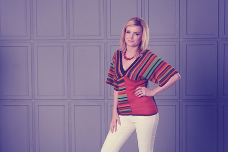 Women posing in studio. She is dressed in a striped knitted blouse and white jeans. She has a necklace on her neck. Clothing in the style of the 1970s. One hand at the waist. Unusual background.の写真素材