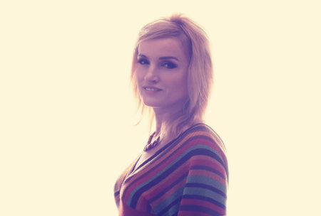 Studio portrait of a beautiful blonde girl. She is dressed in a knitted blouse in a strip, on her neck she has a beautiful necklace. Clothing in the style of the 1970s. A clean background.の写真素材