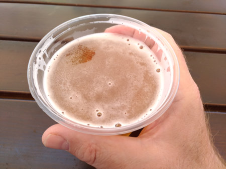Man's hand holding plastic glass with beer against blurred seascape and Street exteriorの写真素材