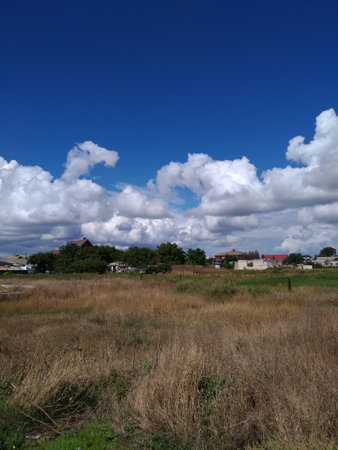 Beautiful clouds over the village houses with red roofs on a blue sky with fild texture in foregroundの写真素材
