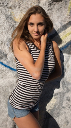 Portrait of a slender young woman in a T-shirt - a vest and short shorts against the wall in an erotic pose. Attractive looking sight, friendliness, cheerfulness, active life position, long, hairの写真素材