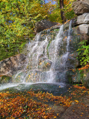 Beautiful waterfall with blurred flowing streams of water against the background of fallen autumn leaves and the green covering of mold stones, nature, Sofiyivka, Ukraineの写真素材