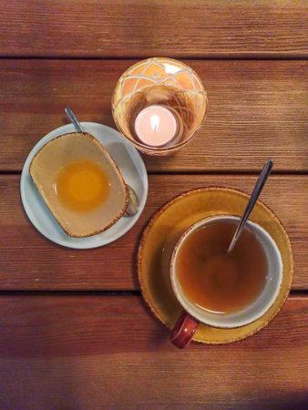 Cafe, table, view from above, cup with tea, saucer with honey and lit candle, romantic atmosphere, vegetarian cuisine, wooden layer, flat layの写真素材