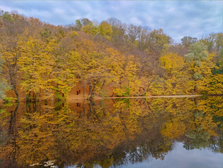 autumn landscape with lake and trees, small people figures in backgroundの写真素材