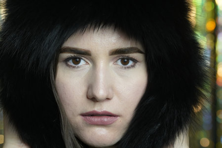 Portrait of casual style woman in winter fur hat close-up, face and hands on glittering backgroundの写真素材