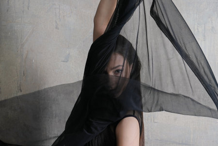Woman dancer portrait in motion with a semitransparent cloth covering face against the wallの写真素材