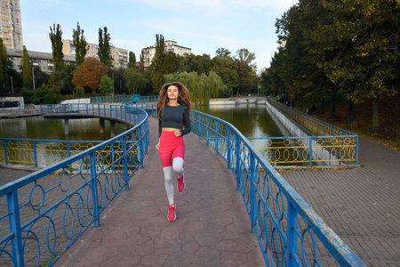 Young Woman Jogging Over a Scenic Bridge in a Beautiful Urban Park Settingの写真素材