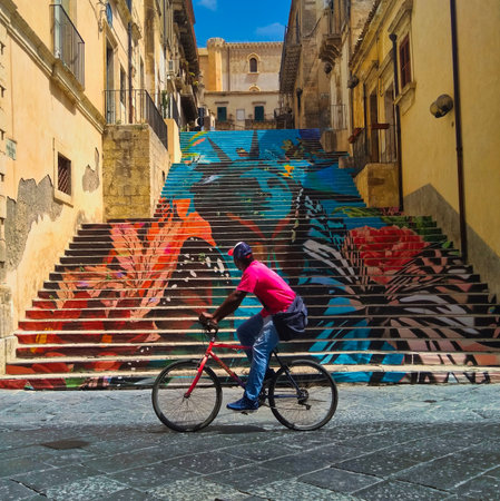 man on bicycle passes in front of a painted stairwayの写真素材