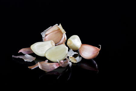 a group of peeled and whole cloves of garlic on a black mirror surfaceの写真素材