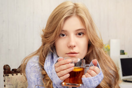 Beautiful blonde girl drinking tea with lemon at homeの写真素材