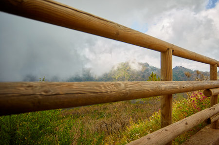 Wooden fence on the backdrop of the rocky mountains, grass, trees and fogの写真素材
