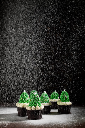 green cakes with the addition of white cream in the form of Christmas trees on a dark textured background are in different order sprinkled with powdered sugarの写真素材