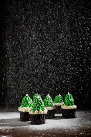 green cakes with the addition of white cream in the form of Christmas trees on a dark textured background are in different order sprinkled with powdered sugarの写真素材