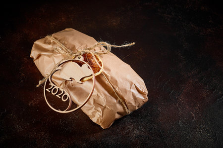 on a dark textural background a gift bundle made of Kraft paper tied with twine with the emblem of the new year symbol mouse made of plywoodの写真素材