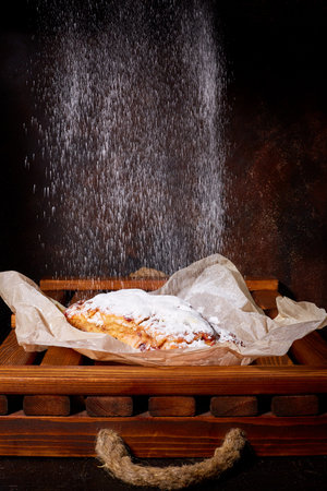 A delicious sweet cake sprinkled with powdered sugar lies on waxed paper and a wooden trayの写真素材