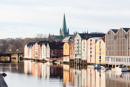 The view across the Nidelva River towards old wooden storehouses in Trondheim, Norway.  In the background is Nidaros Cathedral.のeditorial素材