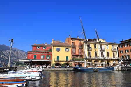 The view across boats moored in the resort town of Malcesine to cafes and restaurants.  Malcesine is on the edge of Lake Garda in North East Italy.のeditorial素材