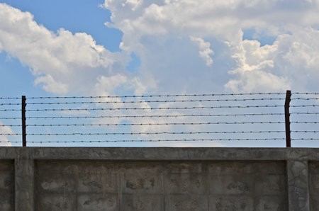 Concrete wall with barbed wires on cloudy skyの写真素材