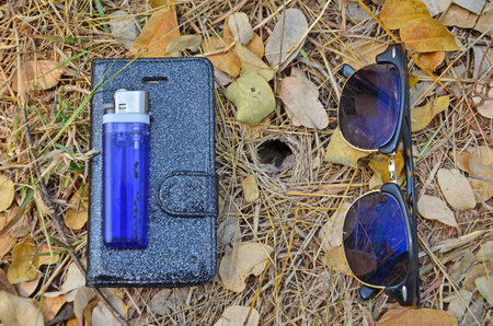 Glasses and mobile phone with lighter on nature floorの写真素材