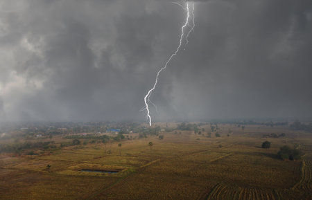 The first rain falls and scary lightning strikes over dry rice fields in Thailandの写真素材