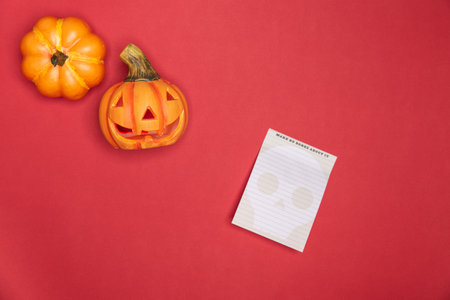Halloween sculpted pumpkin funny and cute face along with full intact pumkin along notes paper. red backgroundの写真素材
