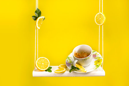 Tea mug sitting on a swing with lots of fresh cut lemon around and beautiful bright yellow backgroundの写真素材