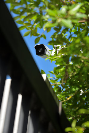 A modern white security CCTV camera on a house gate wall, surrounded by trees, ready to monitor everything happened in front of house gate.の写真素材