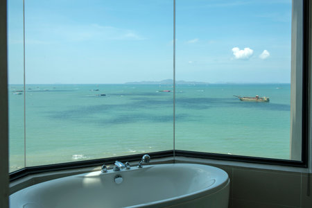 View from a bath room in a luxury hotel, seeing bathtub with a faucet set and a beautiful sea view of Pattaya and islands around.の写真素材