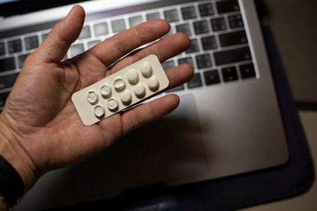 Sick male home office worker taking pills in front of his working space, during his working deadline night. Business or study with stress, late or overwork concepts. Young entrepreneur or student.の写真素材