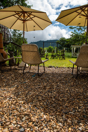 Cozy and relax outdoor chairs with big standing umbrellas in a mountain resort hotel. Seeing a beautiful garden and nice landscape around during a fall season.の写真素材