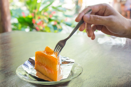 One hands reach to slice orange cake with forkの写真素材