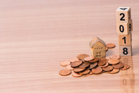 The wooden cube for new year with the house model and coins on wooden backgroundの写真素材
