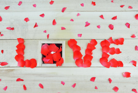 Word love written with rose petals and box with single stone ring on wooden backgroundの写真素材