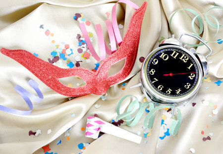 Carnival concept with an alarm clock, mask , confetti, serpentines on golden silk backgroundの写真素材
