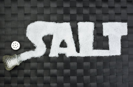 Open saltcellar and word â€œsaltâ€ written with salt on black background