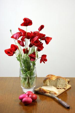 Vase of poppies, red eggs and easter bread on tableの写真素材