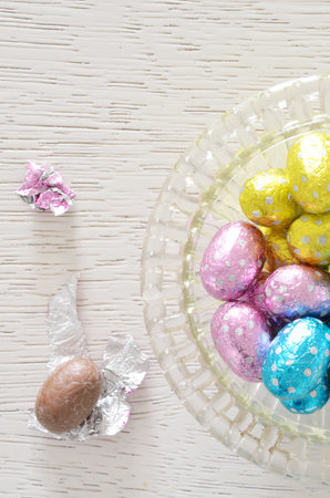 Chocolate egg foil wrapper and chocolate egg beside a glass bowl with foil wrapped Chocolate on...