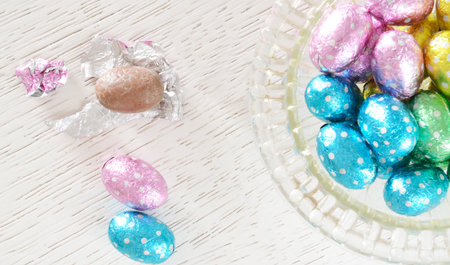 Chocolate egg foil wrapper, an unwrapped chocolate egg  beside a glass bowl with foil wrapped...