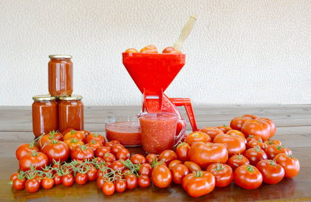 Tomato strainer, fresh tomatoes, fresh and canning tomato sauce and canning on a wooden tableの写真素材