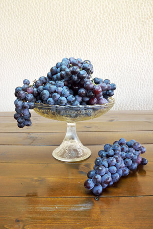 Fruit bowl with grapes and a bunch of grapes on a wooden tableの写真素材