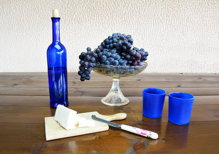 Fruit bowl with grapes, cheese, blue bottle and glasses on a wooden tableの写真素材