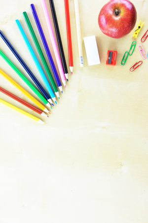 Colored pencils, rubber,sharpener,colored paperpens and an apple on wooden tableの写真素材