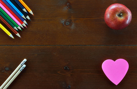 Colored pencils,pencils,an apple and  a heart shaped note sticker on wooden tableの写真素材