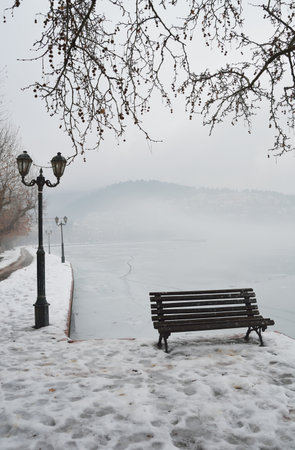 Bench on the banks of frozen lake Orestiada in Kastoria of Greece a overcast foggy dayの写真素材